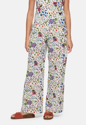 Pantalones blancos de pierna ancha con estampado floral colorido, combinados con sandalias tipo slide de color óxido.