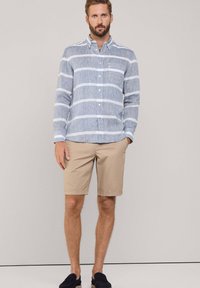 Lichtblauw gestreepte button-up shirt van textielstof, gecombineerd met tan shorts en zwarte instappers. Eenvoudige, casual outfit.