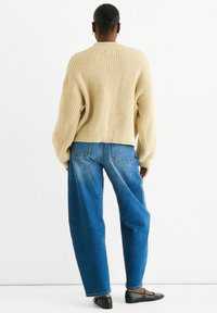 Beige ribbed knit sweater with dropped shoulders, paired with high-waisted blue denim jeans. Footwear features black flats, minimal detailing.