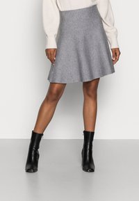 Falda acampanada gris hecha de lana suave, con una cintura alta y una textura suave. Combinada con botas negras hasta el tobillo para un contraste.