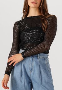 Zwarte top met lange mouwen en een paillettenontwerp met verticale strepen. Gecombineerd met lichtblauwe high-waisted denimbroek.