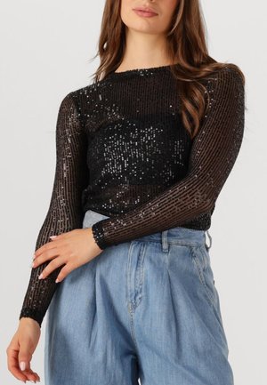 Zwarte top met lange mouwen en een paillettenontwerp met verticale strepen. Gecombineerd met lichtblauwe high-waisted denimbroek.