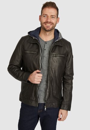Chaqueta de cuero negra con capucha forrada en gris, cremallera frontal y dos bolsillos en el pecho con cremallera. Lleva puesta una camiseta henley gris.