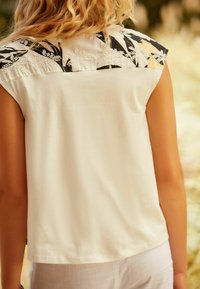 Haut sans manches blanc avec un empiècement noir et blanc à motifs comportant de la broderie ; texture lisse, coupe décontractée, col rond et sans aucune quincaillerie visible.