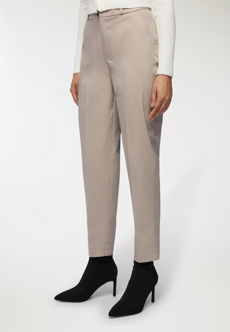 Beżowe dopasowane spodnie o prostym kroju z bocznymi kieszeniami, w zestawieniu z czarnymi szpiczastymi botkami za kostkę. Spodnie są gładkie z delikatnym połyskiem.