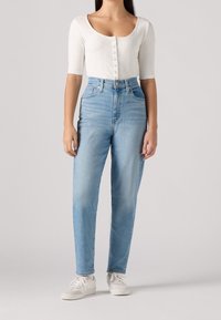 Vit ribbad långärmad topp med knäppning, matchad med ljusblå högmidjade jeans. Foten pryds av vita sneakers.