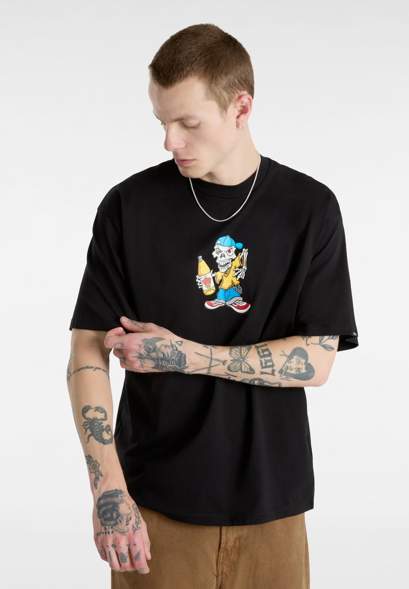 Black short-sleeve t-shirt featuring a colorful graphic of a skeleton holding a drink and food, worn over tan pants.