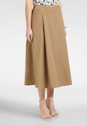 Mujer con falda midi beige en línea A con un pliegue frontal, combinada con zapatos de tacón blancos con correa en el tobillo y una blusa sin mangas con estampado.