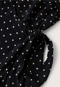 Tissu bleu marine à pois crème, avec un détail de nœud noué. Texture douce avec une finition lisse, adaptée pour une tenue décontractée.