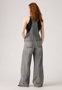 Gray denim overalls with wide legs, adjustable straps, and front and back pockets. Smooth texture and faded finish for a relaxed look.