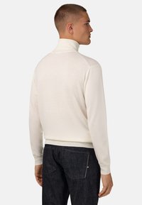 Balts, smalki adīts turtlenecks džemperis ar garām piedurknēm, ar pieguļošu siluetu un ribotiem aprocēm, savienots ar tumšā džinsa biksēm.