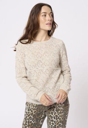 Beżowy sweter o dzianinowym splocie z teksturowanym wzorem w diamenty, okrągłym dekoltem i prążkowanymi ściągaczami, w połączeniu z spodniami w wzór lamparci.