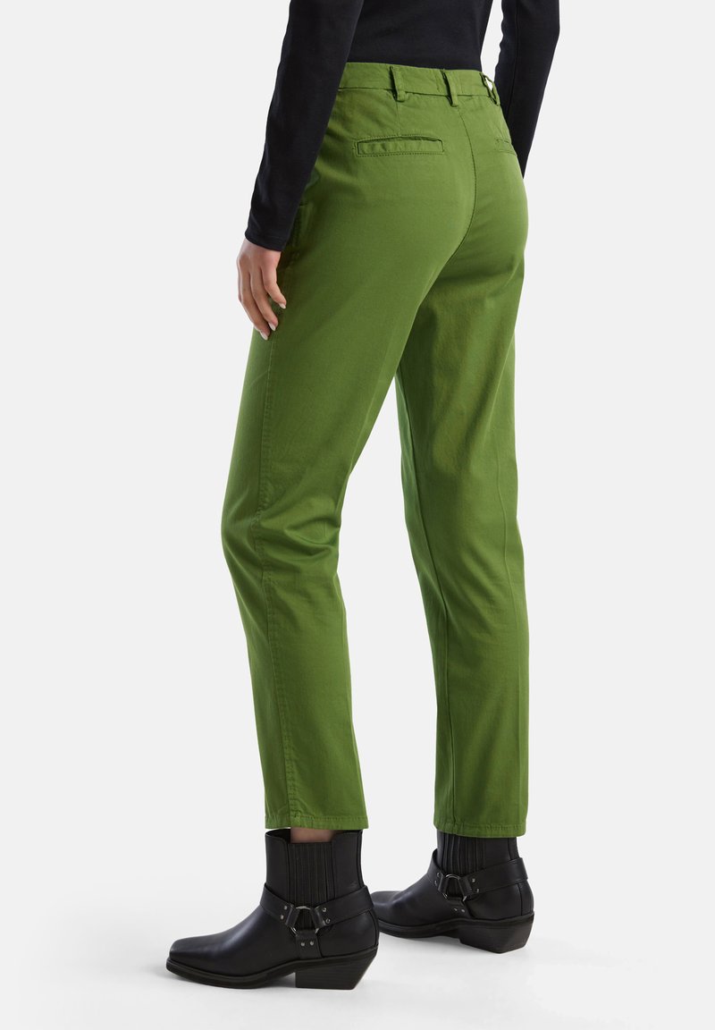 Pantalons en tissu vert avec une coupe ajustée, dotés de poches arrière, d'une texture lisse et associés à des bottines noires.