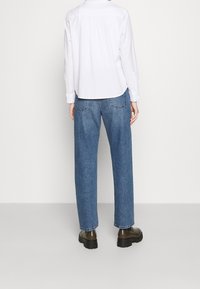 Vit långärmad skjorta, blå vida jeans och kraftiga svarta stövlar. Jeansen har bakfickor; skjortan har en rundad nederkant och knapppdetaljer.