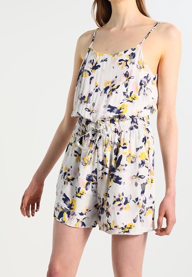 Femme portant un combishort sans manches à imprimé floral avec une ceinture ajustable à la taille en blanc, jaune, marine et rose.