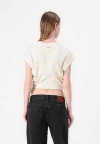 Top corto a maniche corte di colore crema con maniche arrotolate, abbinato a jeans neri a vita alta con una patch in pelle marrone e tasche posteriori.