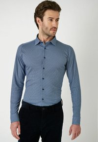 Lange mouw button-down shirt in blauw met een klein geometrisch patroon, met een kraag en zwarte knopen, gecombineerd met donkere broeken.