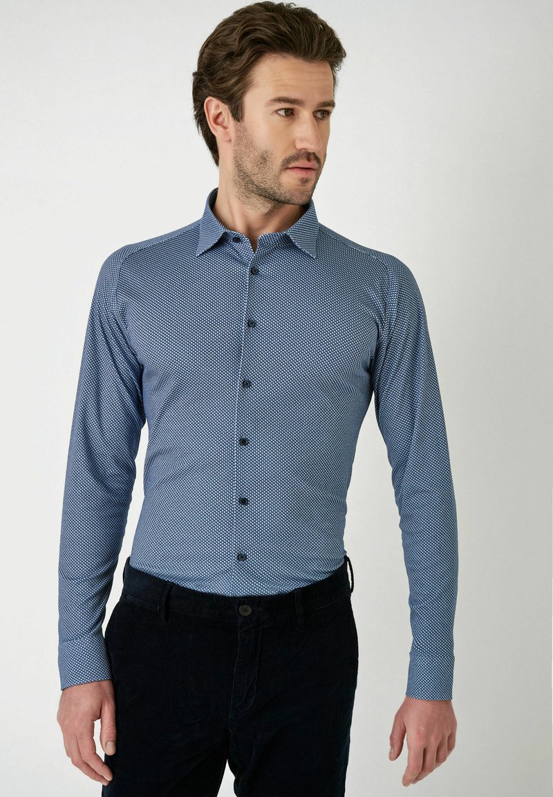 Lange mouw button-down shirt in blauw met een klein geometrisch patroon, met een kraag en zwarte knopen, gecombineerd met donkere broeken.