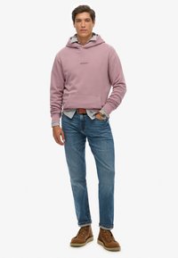 Fioletowa bluza z kapturem z przednią kieszenią, nałożona na jasnoniebieską koszulę. Noszona z niebieskimi dżinsami i brązowymi sznurowanymi butami. Zegarek na lewej ręce.