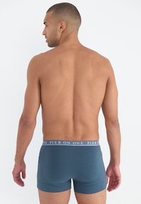 Männliche Boxershorts in dunklem Teal mit weichem Stoff. Mit einem elastischen Taillenbund in Marineblau, der das Logo und den Text "PIER ON ONE" trägt.