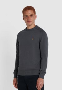 Grauer Strickpullover mit Rundhalsausschnitt, ausgestattet mit gerippten Bündchen und Saum sowie einem kleinen orangefarbenen Logo auf der Brust. Glatte Textur und figurbetontes Design.
