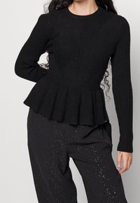 Czarny, prążkowany top peplum z długim rękawem, z teksturowanym wzorem i dopasowaną górą, która rozszerza się w talii.