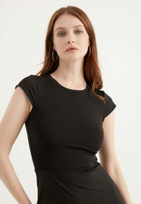 Schwarzes, tailliertes Kleid mit rundem Ausschnitt und kurzen Ärmeln, aus glattem Stoff gefertigt. Verfügt über eine geraffte Detail am Taillenbereich.