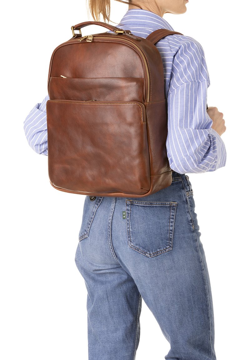 Sac à dos en cuir marron avec une texture lisse, deux zips et une poche frontale. Il possède des bretelles réglables et une poignée supérieure.