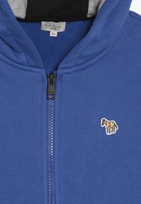 Modrá mikina s kapucí na zip vyrobená z měkké látky, s vyšitým multicolor designem koně na levé straně hrudi a černou vnitřní kapucí.