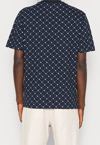 Camiseta de manga corta azul marino hecha de algodón, con un patrón de diamantes blancos repetido. Diseño de cuello redondo simple, ajuste relajado.