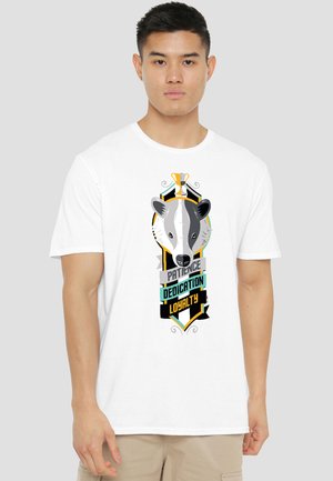 Man wearing a white t-shirt with a badger illustration and the words "Patience," "Dedication," and "Loyalty" on the front.