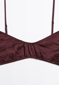 Soutien-gorge bordeaux en tissu lisse, avec des fines bretelles, un centre froncé et des coutures discrètes le long des bords.