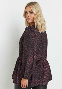 Tumman leopardikuosiset pusero, jossa on pitkät puffihihat, kerätty vyötärö ja rento peplum-siluetti. Kankaan pinta on sileä.