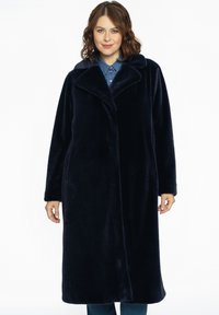 Lakeret frakke i navyblåt imiteret pels med bred krave, lange ærmer og sidelommer, der har en blød tekstur og knælængde design.
