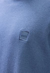 Suéter azul malhas com um acabamento texturizado e um retângulo destacável com a palavra "BOSS" em uma cor azul mais clara.