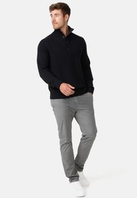 Suéter negro de punto con cuello alto y tapeta de tres botones, combinado con pantalones gris claro y zapatillas blancas. Diseño simple, tejido texturizado.