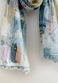 Lekki, wzorzysty szalik z ilustracjami miejskiego krajobrazu w pastelowych kolorach. Materiał wydaje się miękki, ma przezroczystą teksturę i frędzlowe wykończenie.