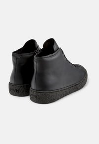 Zapatos altos de cuero negro con una suela de goma negra texturizada. Cuenta con una puntera redondeada y un mínimo detalle de cordones.