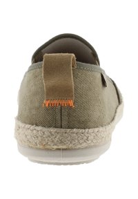 Zapato tipo slip-on de lona verde con suela de yute trenzada, que presenta un tirador en la parte trasera de tela marrón con costuras naranjas. Textura suave, forma redondeada.