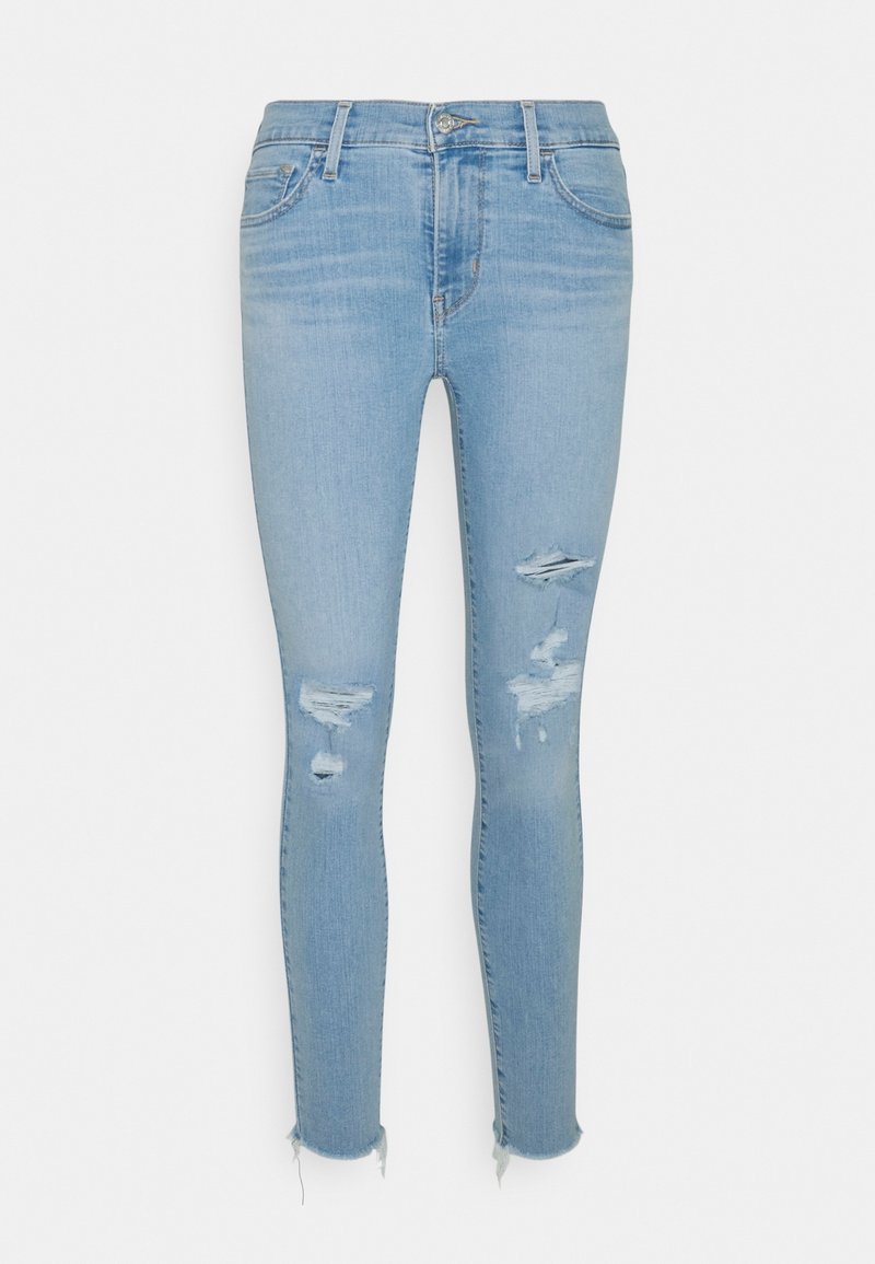 Světlé modré skinny džíny vyrobené z denimu, s vysokým pasem, s různými otvory, trhlinami na kolenou a roztrhaným lemem.