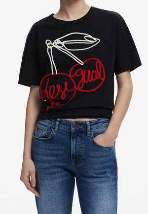 Czarny krótki t-shirt z białym i czerwonym wzorem wiśni oraz słowem „Desigual” uformowanym w wiśniach, noszony z niebieskimi dżinsami.