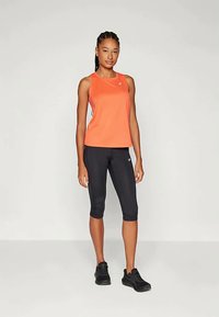 Oranžikas ilma varrukatop, millel on ümmargune kaelus, koos mustade capri legginsitega. Riietus on sujuva disainiga ja kerge tekstuuriga.