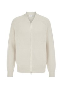 Helebeežilt beezipukasard, valmistatud soonilise tekstuuriga kangast, raglaanvarrukatega ja ääristatud kraega, varustatud hõbedase luku ja ilma lisakaunistusteta.