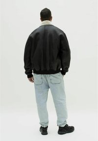 Sort læder bomberjakke med krave af hvid fårskindslook, ribbede manchetter, parret med lyseblå jeans og sorte sneakers.