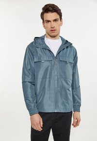 Lys blå zip-up jakke lavet af glat, vandafvisende stof. Har hætte, to brystlommer og elastiske manchetter.