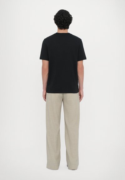 T-shirt noir à manches courtes avec col rond, associé à un pantalon large beige clair, présentant une texture lisse et un design minimal.