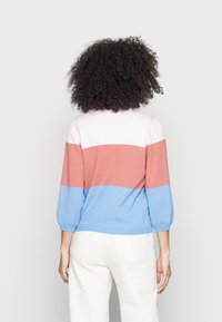 Color-blocked sweater in pink, orange, and blue, featuring a textured knit and three-quarter sleeves, worn with white pants.