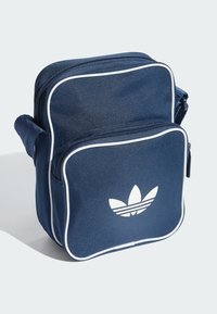 Torba preko ramena tamnoplave boje izrađena od teksturiranog tkanja, s bijelim prugastim logotipom, kontrastnim bijelim oblogama i glavnim pretincem zatvorenim patentnim zatvaračem.