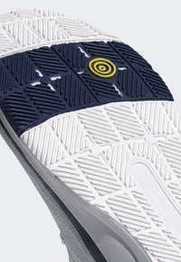 Bílá podrážka tenisky s texturovanou gumou, námořnický střed s geometrickými vzory a výrazným žlutým kruhovým akcentem.