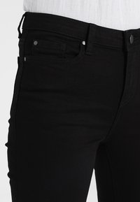 Los vaqueros negros de denim presentan un corte ajustado, un diseño de cinco bolsillos, detalles en hardware plateado y una textura suave.